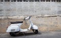 White Classic Vespa scooter stands parked near the concrete old