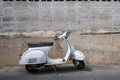 White Classic Vespa scooter stands parked near the concrete old