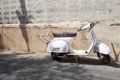 White Classic Vespa scooter stands parked near the concrete old