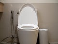 White clean ceramic toilet bowl, front view with silver bidet shower or health faucet beside the bin in modern bathroom. Royalty Free Stock Photo
