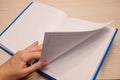 White clean notebook in a cage for notes lies on a wooden background and a woman`s left hand flips through the sheets of the Royalty Free Stock Photo