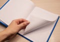 White clean notebook in a cage for notes lies on a wooden background and a woman`s left hand flips through the sheets of the Royalty Free Stock Photo