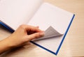 White clean notebook in a cage for notes lies on a wooden background and a woman`s left hand flips through the sheets of the Royalty Free Stock Photo