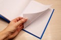 White clean notebook in a cage for notes lies on a wooden background and a woman`s left hand flips through the sheets of the Royalty Free Stock Photo