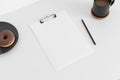 White clipboard mockup with a coffee, donuts and a pen on a white table