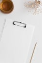 White clipboard mockup with a cup of tea and gypsophila on a white table