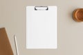 White clipboard mockup with a cup of tea and workspace accessories on a beige table