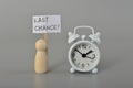 White clock and wooden doll figure hold sign board with text LAST CHANCE