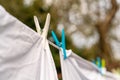 White clothes hung out to dry on a washing line and fastened by the clothes pegs in the bright warm sunny day. Blurred garden at Royalty Free Stock Photo