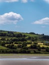 A white cloud in a blue sky. Trees on the slope of a green hill. Picturesque summer landscape. Irish nature. Green hill under blue