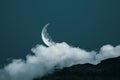 A white cloud in the shape of a crescent moon on a dark blue sky with a black mountain background, clouds are in front of it, Royalty Free Stock Photo