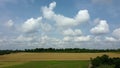 White clouds on blue sky over yellow ripened wheat field green trees Royalty Free Stock Photo