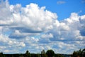 White clouds float across the blue sky, forest and field. Beautiful atmospheric phenomenon. Natural horizontal background Royalty Free Stock Photo