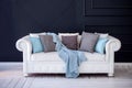 White coach with a grey and blue pillows and woolen blanket standing on a white wooden floor against dark blue wall