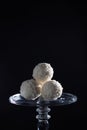 white coconut balls of candy on a glass luxury stand on a black background, exquisite dessert, heavenly delight