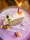 White coconut cake with candles in a purple dish on a wooden table