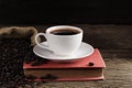 A white coffee cup with black coffee is placed on a red book and a large number of roasted coffee beans are placed around on a Royalty Free Stock Photo