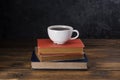 White coffee cup with dark black coffee And old books And the clock is arranged on an old wooden table and a black wooden wall Royalty Free Stock Photo