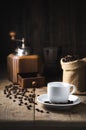 The white coffee cup on the dish. top the old wood table has coffee vintage grinder beans and Moka pot as dark tone background the Royalty Free Stock Photo