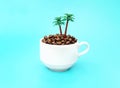 White coffee cup full of roasted coffee beans and toy palm trees isolated on a light blue background. Royalty Free Stock Photo