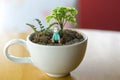 `White coffee cup with little tree and small doll