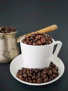 White coffee cup and saucer; coffee beans scattered on the table. In the background is a cezve. Black background. Royalty Free Stock Photo