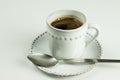 A white coffee cup full of black coffee and tea spoon on white saucer standing on white table as background. Royalty Free Stock Photo