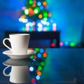 White coffee cup and saucer on a glass table on the background colorful bokeh.