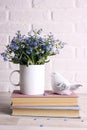 White coffee mug with bouquet of forget-me-not flowers, books and bird on the white brick wall background Royalty Free Stock Photo