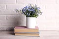 White coffee mug with bouquet of forget-me-not flowers and books on the white brick wall background Royalty Free Stock Photo