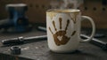Coffee mug with a dirty handprint on it in a workshop. Royalty Free Stock Photo