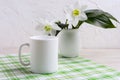White coffee mug mockup with lily in vase on green checkered napkin Royalty Free Stock Photo