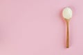 White collagen powder on a wooden spoon on a pink background. Skin care, rejuvenation. Copy space.