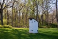 White colonial Pennsylvania outhouse in grass field with tall trees