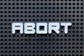 White alphabet with word abort on black pegboard background