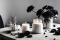 White color jar with black flowers on the table, a candle near the jar with black theme