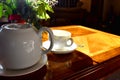 White color of Teapot and a cup of hot tea on wooden table and bright light from sun. Traditional english tea in afternoon. Royalty Free Stock Photo