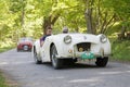 White color Triumph TR2 classic car from 1953 driving on a country road