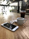 White colored Apple brand Iphone 8 Phone and Airpods 2 on a wooden table with charging box and cup of espresso