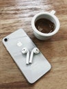 White colored Apple brand Iphone 8 Phone and Airpods 2 on a wooden table with cup of espresso