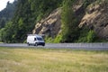 White compact cargo mini van driving to point of business on the road with rock wall