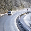 White compact commercial cargo mini van running on wet snowy winter road with trees in snow Royalty Free Stock Photo