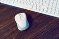 A white computer mouse and keyborad on a wooden desk