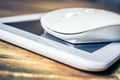 White Computer Mouse On Top Of A White Tablet On Wooden Table