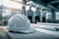 White construction helmet resting on architectural blueprints with engineers in safety gear discussing project details in blurred Royalty Free Stock Photo