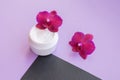 White container with cream for face and body with three magenta colored orchid flowers on purple and black background. Royalty Free Stock Photo