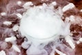 White cool dry ice frozen carbon dioxide with smoke effect in the glass bowl on the dark brown wooden background.