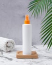 White cosmetic bottle orange spray pump with towels and a palm leaves on a wooden table and concrete wall. Sun protection and Royalty Free Stock Photo