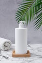White cosmetic dispenser bottle mockup with towels and a palm leaves on a wooden table and concrete wall. Beauty skin care product