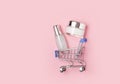 White cosmetic jars with cream lie in a shopping trolley on a pink background. Online home shopping